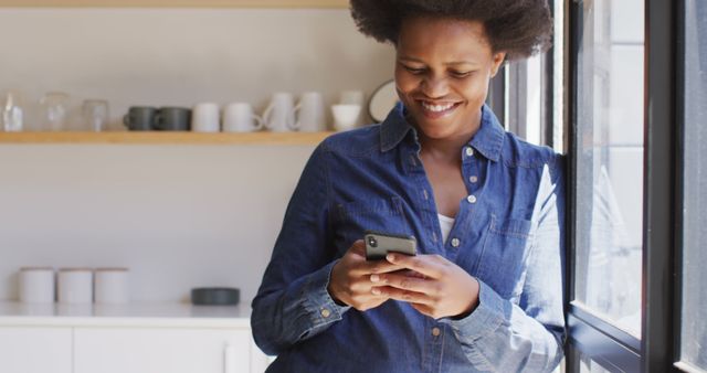 Happy african american woman using smartphone in kitchen. domestic lifestyle, spending free time at home.