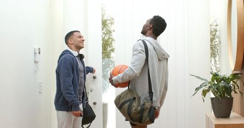 Smiling diverse male friends heading out for basketball in modern minimalist home entryway