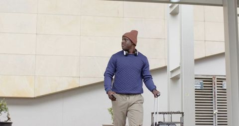 Urban traveler walking with rolling suitcase wearing beanie and headphones