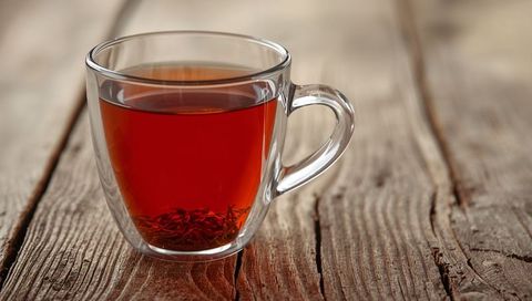 Double-Walled Glass Mug with Amber Tea and Loose Leaves on Rustic Wood Planks