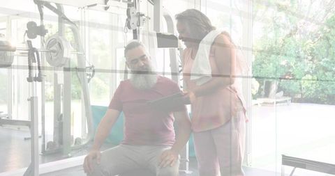 Senior man reviewing tablet with trainer in bright home gym overlooking backyard pool