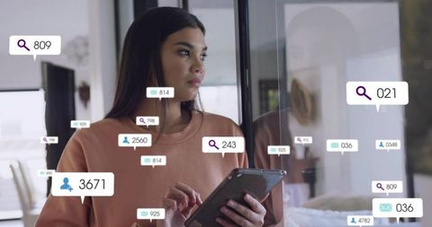 Mid adult woman holding tablet by glass door with floating social notification badges