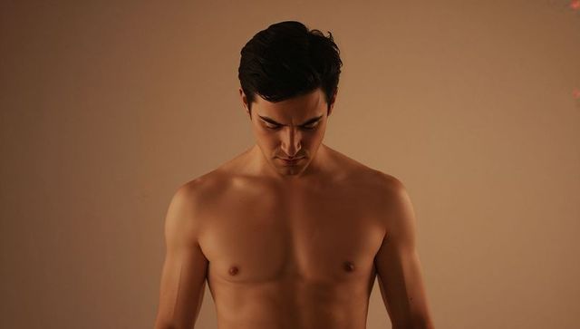 Bare-chested man standing bowing head and gazing downward with warm beige lighting
