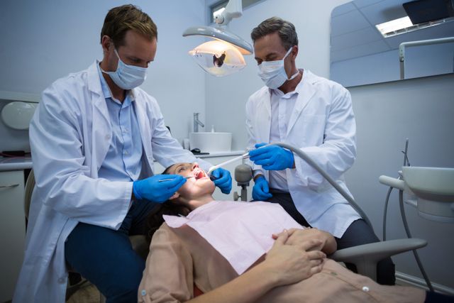 Dentists examining a female patient with tools at dental clinic