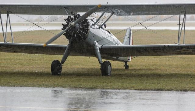Vintage biplane on wet grass in heavy rain showing radial engine and two-blade propeller