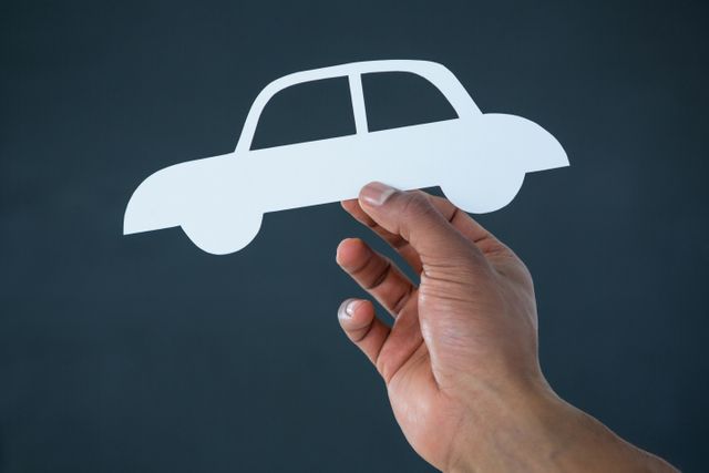 Hand of businessman holding paper cut out car against grey background