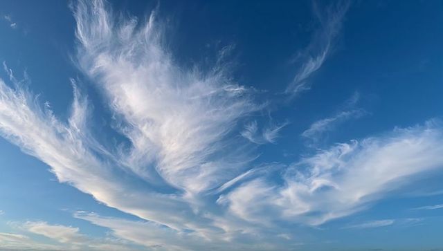 Sweeping Fan-Shaped Cirrus Clouds Across Expansive Blue Sky with Wispy Horizon Bands