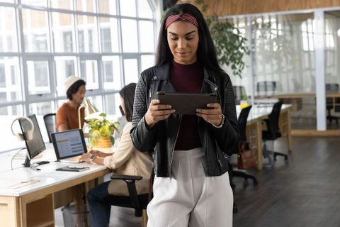 Confident indian woman holding tablet in open-plan office with diverse team collaborating