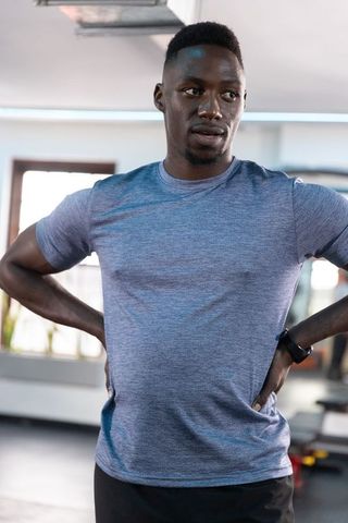African american man standing hands on hips in gym wearing smartwatch and athletic t-shirt