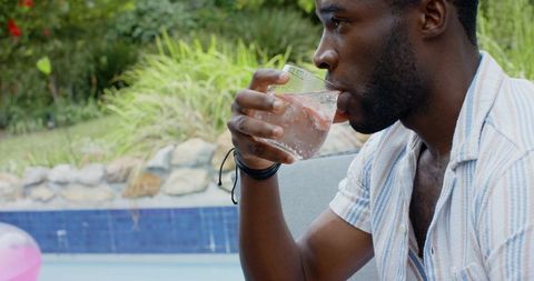 African american man sipping iced drink relaxing on poolside lounge chair in backyard