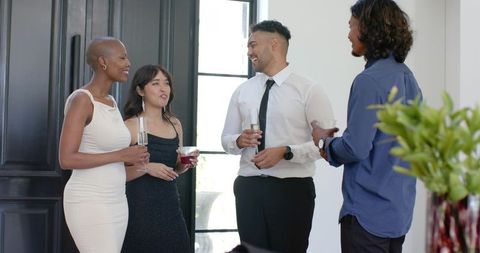 Group chatting at cocktail party in modern foyer holding champagne flutes and cocktails