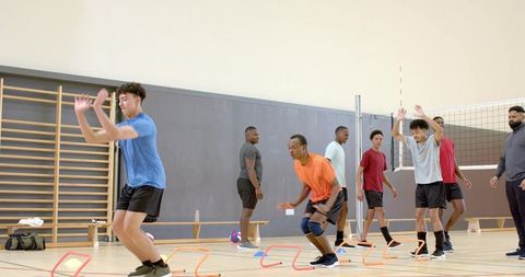 Diverse male volleyball team practicing agility and blocking footwork with hurdles in gym