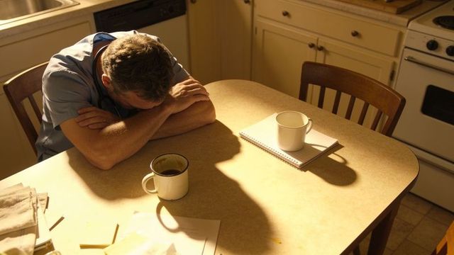 Exhausted doctor leaning, resting head on kitchen table after long shift with coffee
