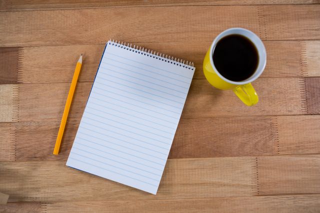 Coffee mug with notepad and pencil on wooden table