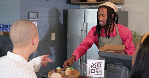 African american barista serving cupcakes at rustic industrial cafe counter with qr code