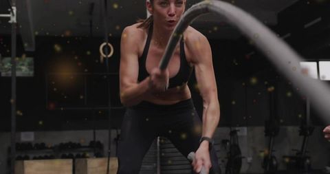 Mid-adult woman powering battle ropes during intense hiit strength training