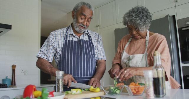 This vibrant image depicts a joyful African American senior couple in a modern kitchen, engaged in preparing a meal together. The couple is smiling and enjoying each other's company while handling fresh vegetables, emphasizing themes of healthy living, active retirement, and family bonding. Intended for use in advertisements, articles, and promotional materials related to health, nutrition, elderly lifestyle, and family wellness.