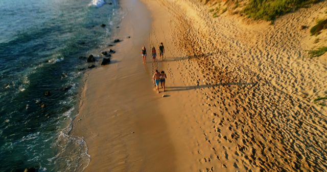 A group of friends is walking on a sandy beach at sunset, leaving footprints in the sand. The ocean waves gently lap at the shore. This image can be used for themes of friendship, summer vacations, and peaceful coastal scenes. Ideal for travel blogs, vacation advertisements, and social media posts about beach outings.