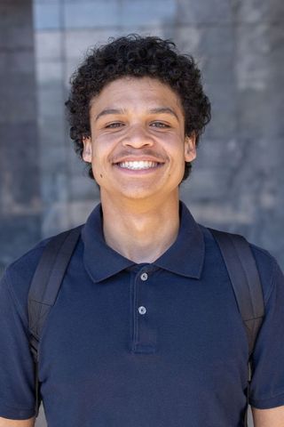 Confident african american student smiling with backpack on urban campus portrait daylight headshot