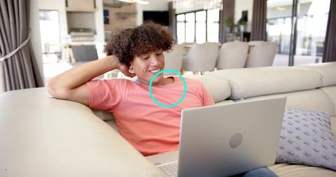 Relaxing young man lounging on couch using laptop in bright modern living room