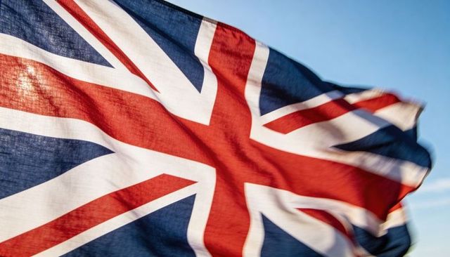 Waving union jack closeup woven texture and stitching pale blue sky rippling in wind