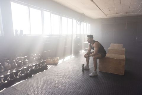 Man sitting on plyometric boxes in sunlit industrial gym, resting after intense workout