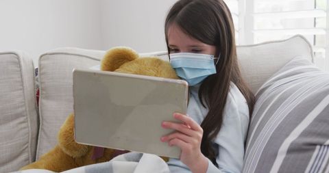 Young Girl with Teddy Bear Using Tablet in Pandemic Setting