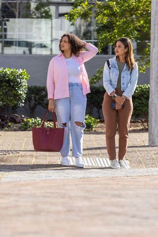 African american friends standing in urban plaza holding burgundy tote and smartphone