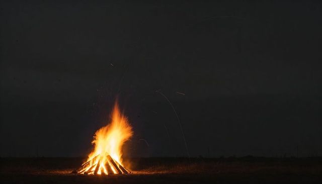 Night bonfire blazing on open field with teepee log fire and flying embers