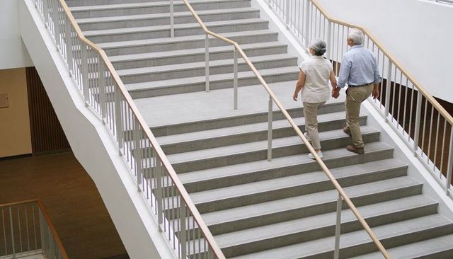 Senior couple holding hands walking up modern staircase in bright atrium for active aging
