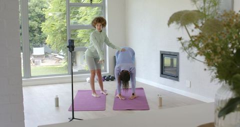 Yoga instructor guiding student through forward fold at-home session with tripod filming