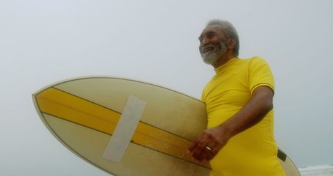 Smiling Senior Surfer Holding Surfboard on Cloudy Beach