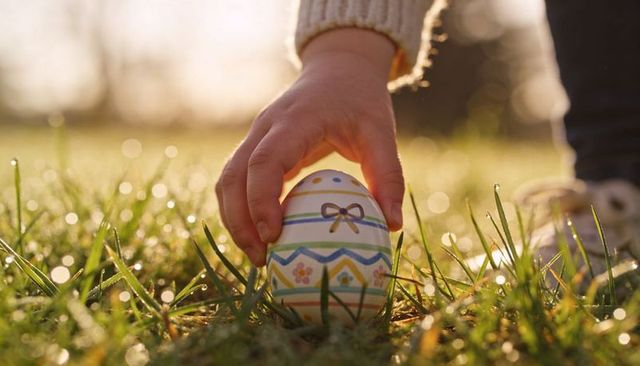 Child holding decorated easter egg on dew-kissed grass at sunrise with soft bokeh
