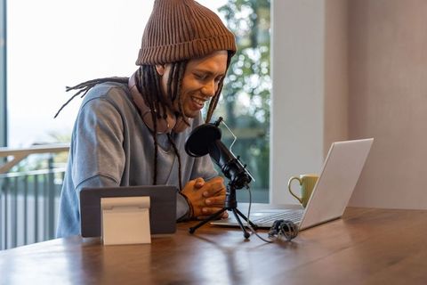 African american creator recording podcast at home workspace with laptop and microphone