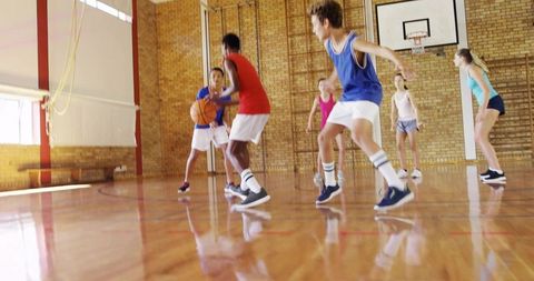 Teenagers dribbling and defending on sunlit school gym hardwood basketball court action