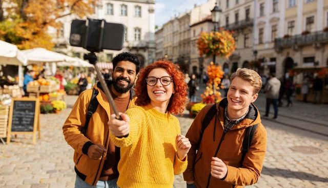 Friends taking autumn selfie in historic european market square with vibrant fall stalls