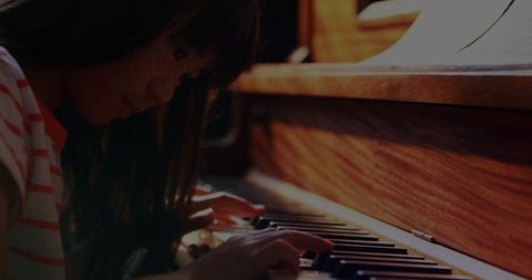 Young asian girl practicing on wooden piano with sheets displayed