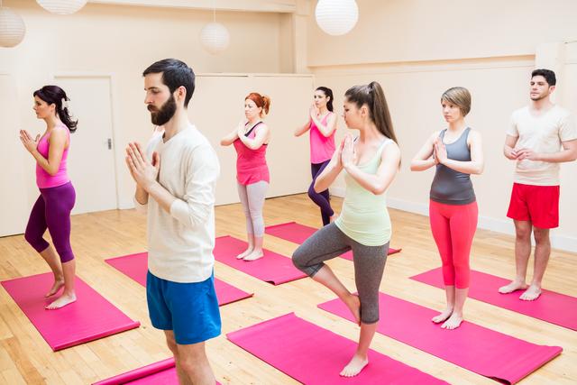 Group of people performing tree-pose yoga exercise in the fitness studio