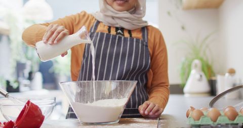 Smiling woman in hijab baking with flour and milk in kitchen