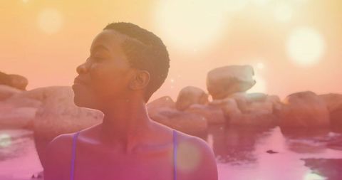 Sunset solitude: short-haired woman standing at rocky coastline with warm lensflare glow