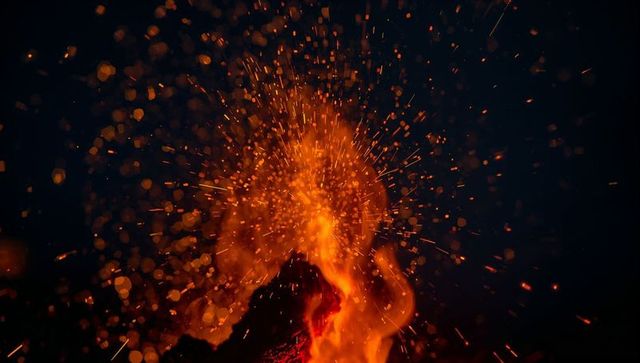 Glowing embers exploding upward from campfire sparks against dark night sky with bokeh