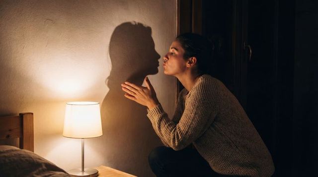 Woman creating shadow profile on wall with warm lamp light, intimate night moment