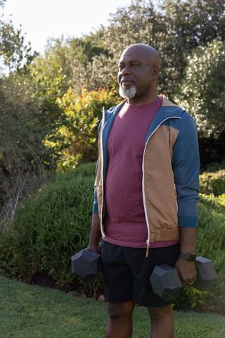 Senior Man Exercising with Dumbbells in Well-kept Garden Outdoors