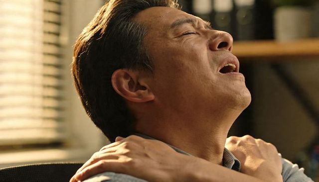 Middle-aged asian man rubbing shoulders in office chair showing neck and shoulder pain