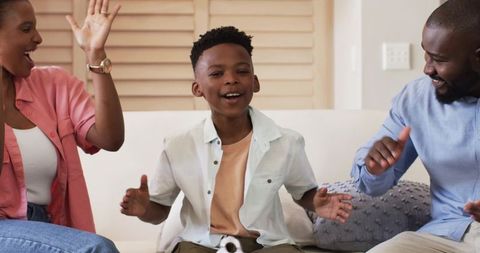 African American family clapping and encouraging child singing on sofa in cozy living room