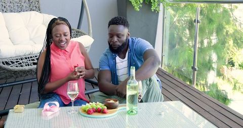 Joyful Couple Enjoying Wine and Fruit on Modern Balcony Retreat