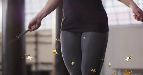 Athletic woman jumping rope with gold star confetti, backlit gym cardio motion and energy