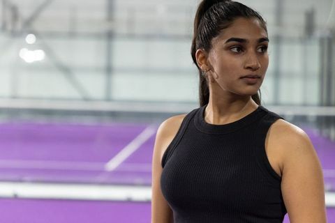 Indian female athlete standing at indoor court wearing black top against purple backdrop