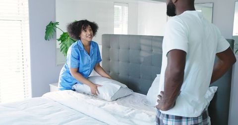African American couple making bed and chatting in modern bright bedroom