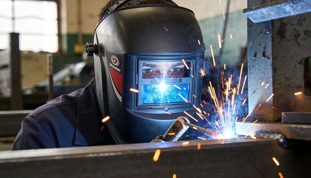 Close-up industrial welder welding steel beams with auto-darkening helmet producing bright sparks